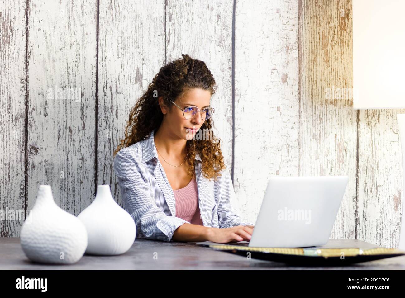 Giovane donna che indossa bicchieri seduti a un tavolo da pranzo remoto lavorare su un computer portatile da casa durante il blocco per La pandemia di Covid-19 Foto Stock