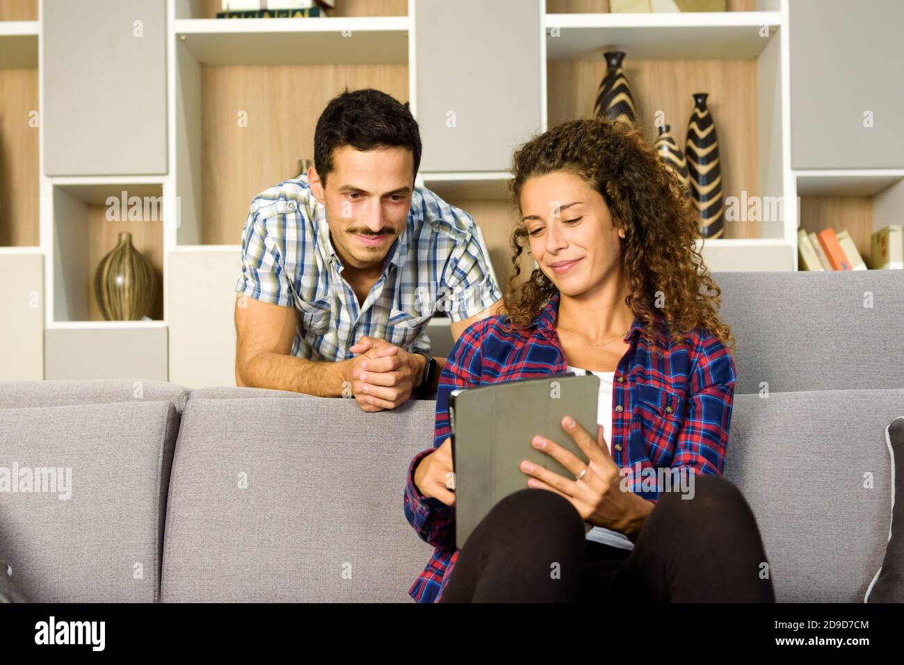 Un giovane coppia trasmette contenuti multimediali in streaming su un tablet-pc seduto insieme a guardare esso nel loro soggiorno con sorrisi soddisfatti in un concetto di intrattenimento personale Foto Stock
