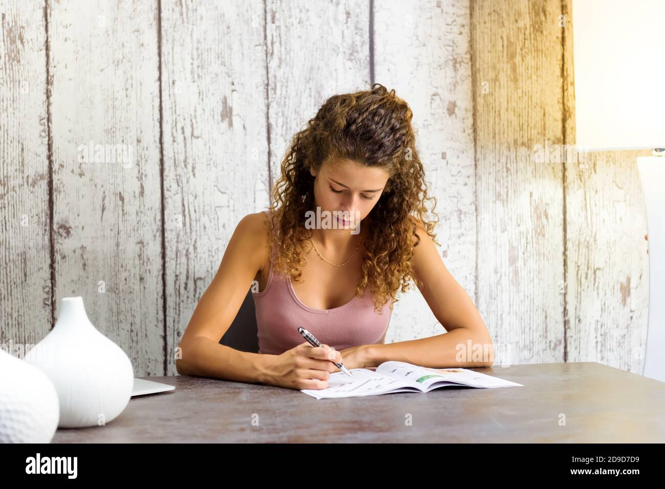 Giovane donna seduta riempiendo in cruciverba puzzle in una rivista o libro che si concentra sulla risoluzione degli indizi seduti ad un tavolo a casa Foto Stock