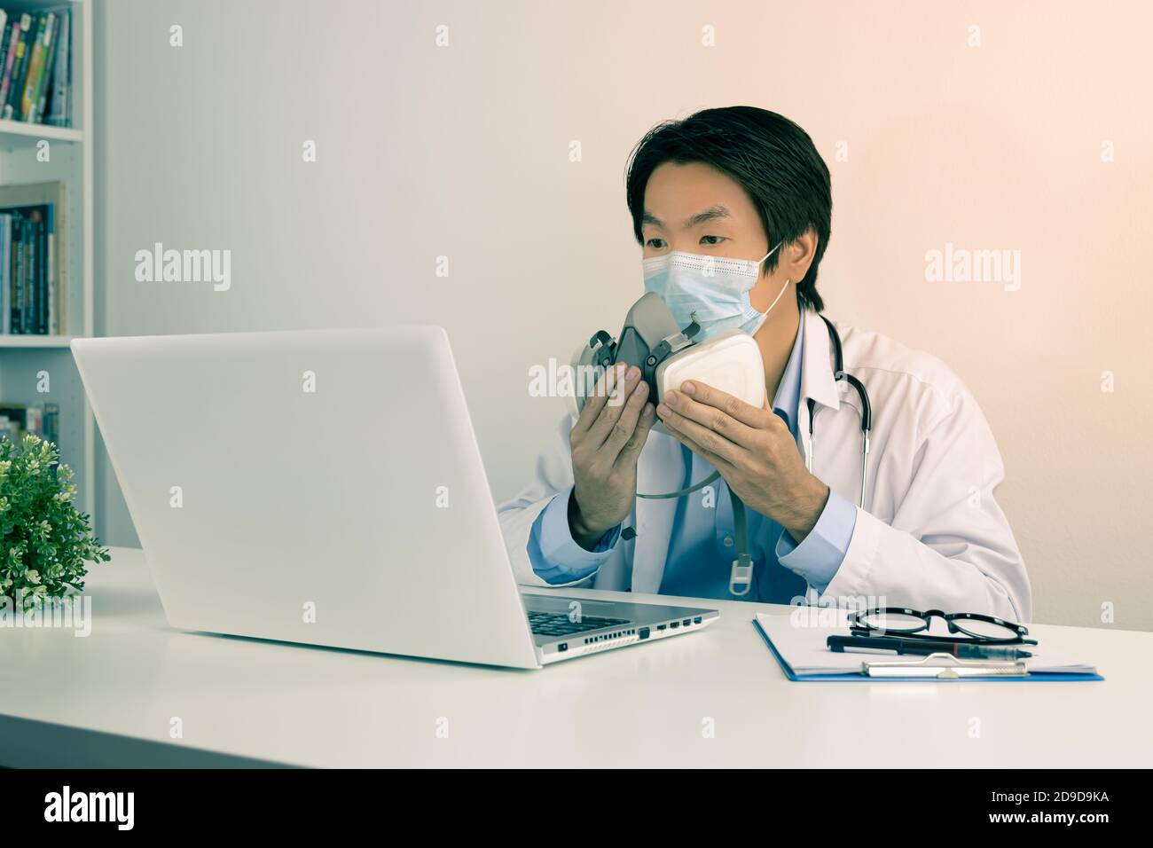 Giovane uomo medico asiatico in camice da laboratorio o camice con Stetoscopio maschera di usura del viso dimostrare maschera di filtro uso con il paziente Tramite computer portatile in Office in Foto Stock