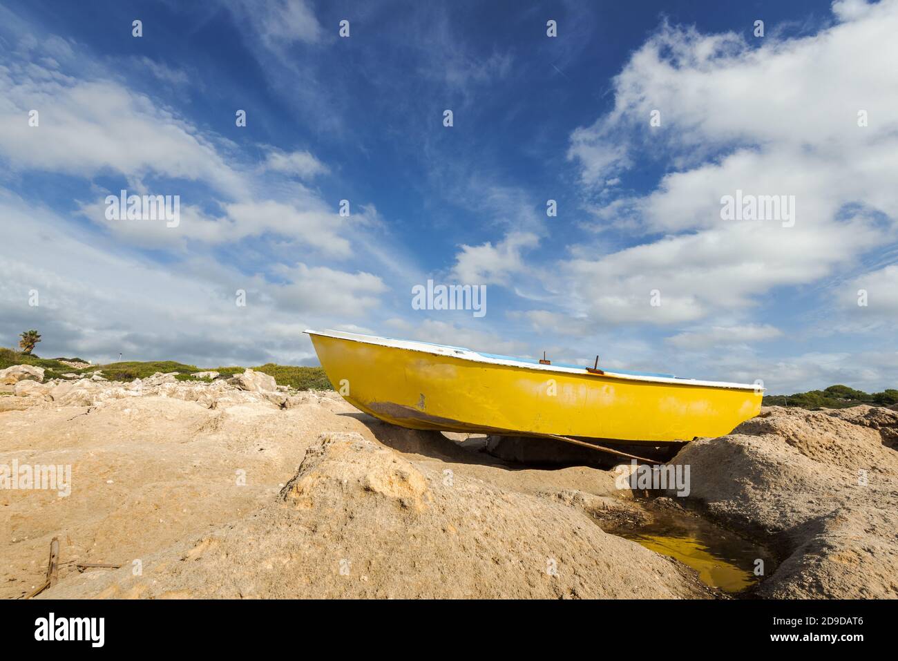 barca di legno giallo intrecciata sulla riva sassosa con drammatico cielo nuvoloso dopo la tempesta . Minorca, Spagna Foto Stock