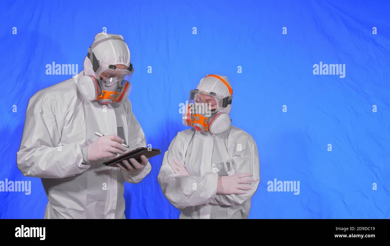 Lo scienziato virologo in respiratore scrive in un computer tablet con stilo. Uomo e donna che indossano una maschera medica protettiva. Tasto Chroma blu. Foto Stock