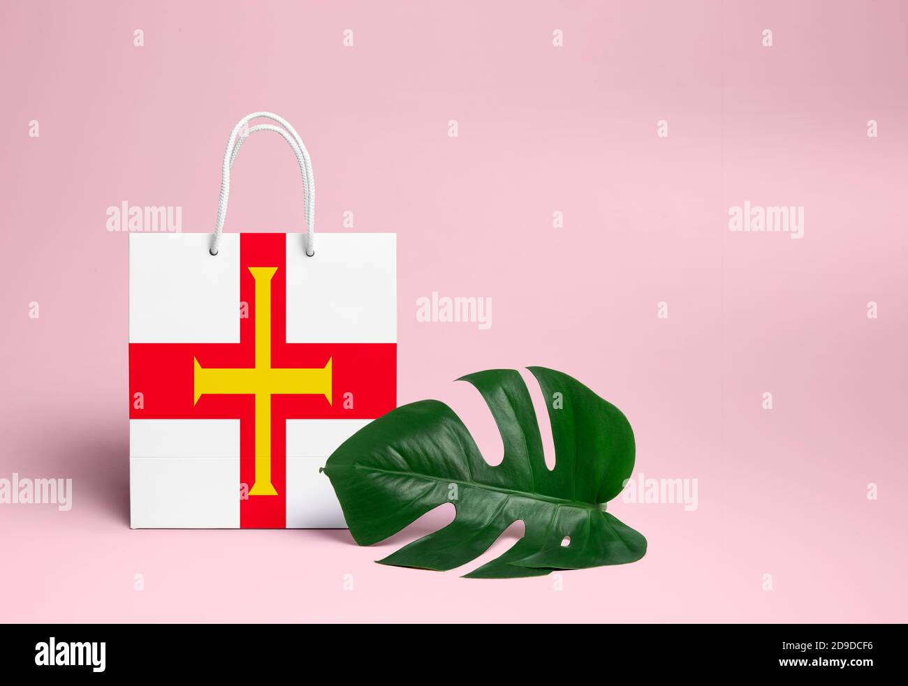 Concetto di shopping Guernsey. Borsa di cartone nazionale con foglia di monstera e sfondo rosa. Tema di shopping online. Foto Stock