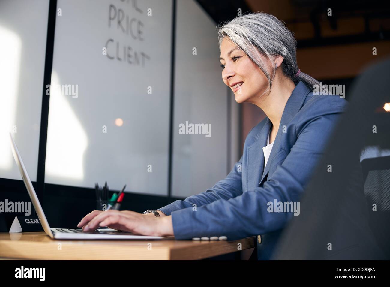 Donna allegra che lavora su un computer portatile moderno in ufficio Foto Stock