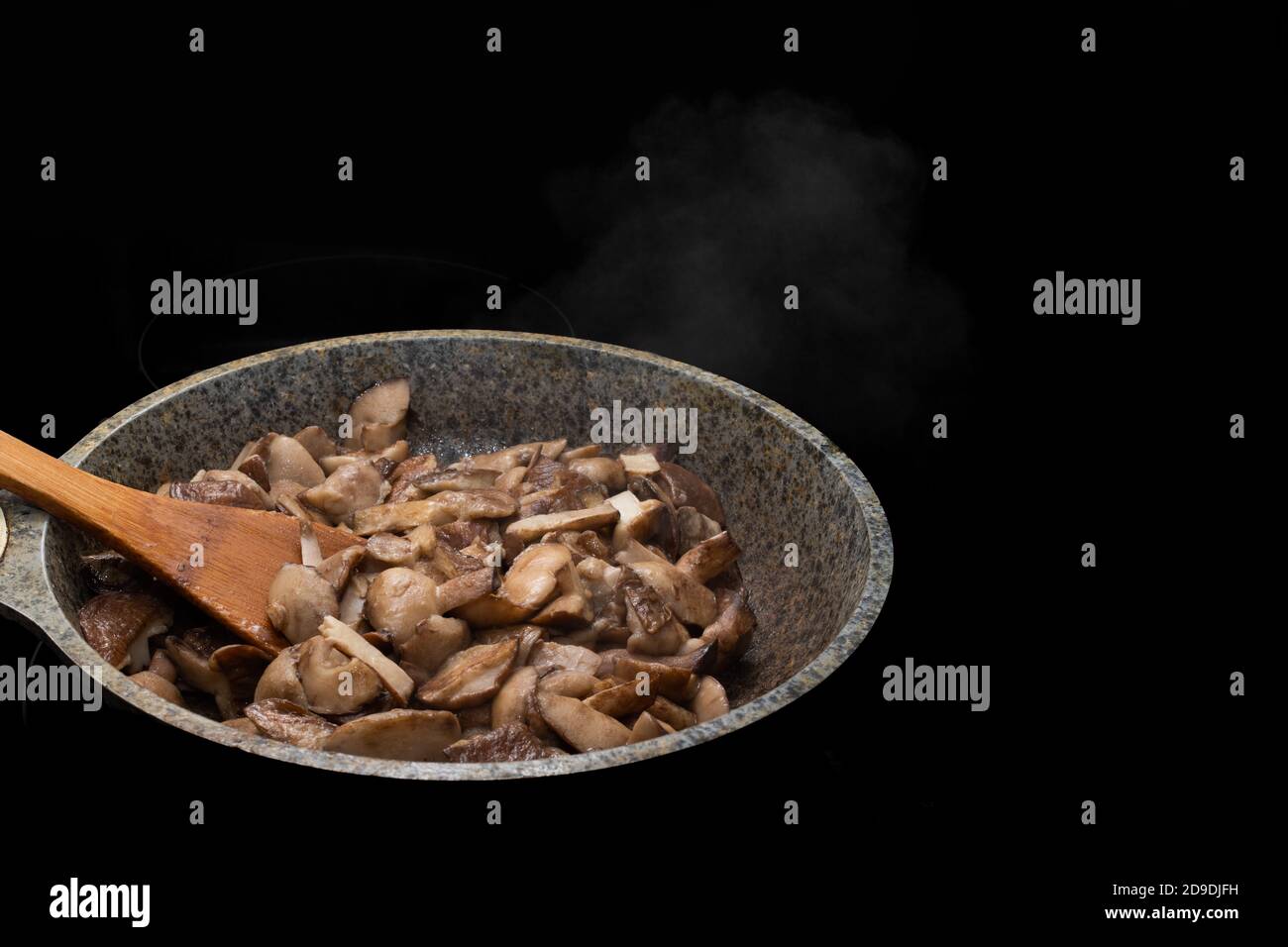 Primo piano di un cucchiaio di legno e funghi fritti o stufati in una padella, il vapore sale dai funghi caldi Foto Stock