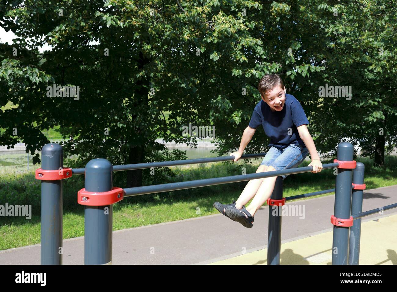 Ragazzo allena i muscoli addominali su barre irregolari nel parco Foto Stock Ragazzo allena i muscoli addominali su barre irregolari nel parco Foto Stock