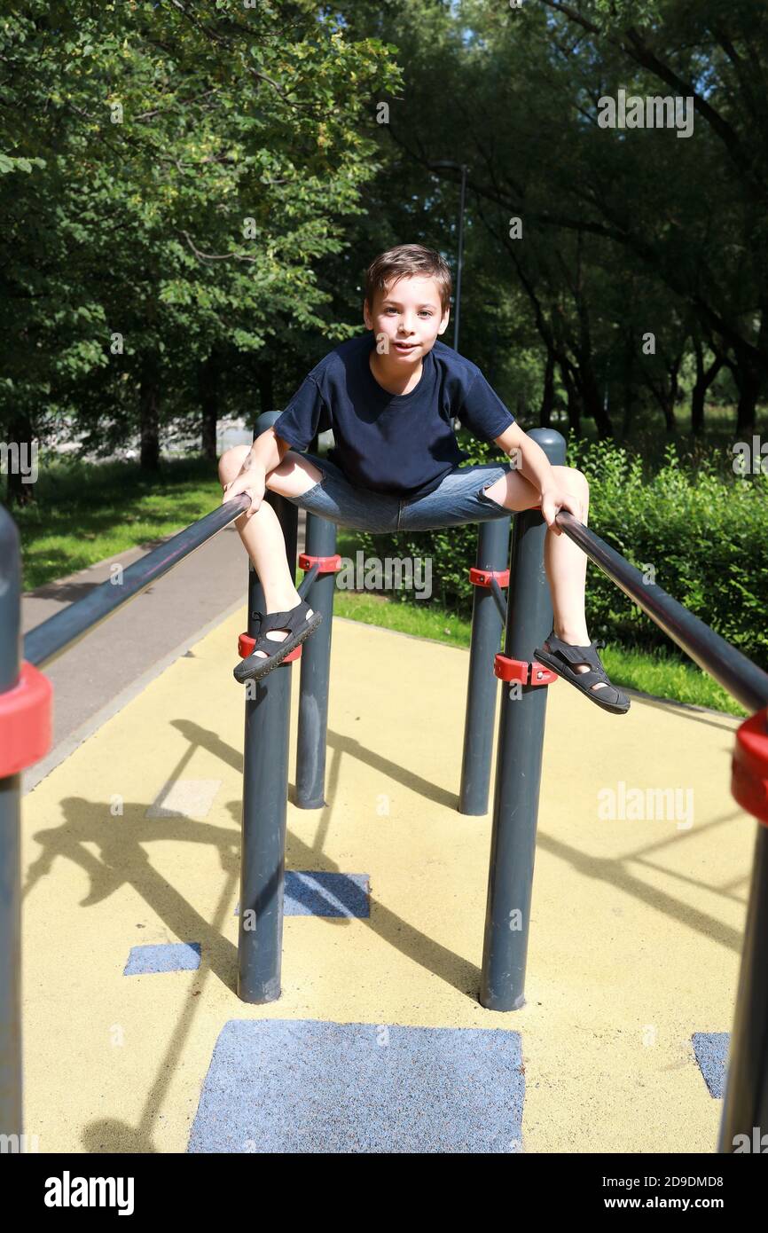 Il bambino allena i muscoli addominali su barre irregolari nel parco Foto Stock Il bambino allena i muscoli addominali su barre irregolari nel parco Foto Stock