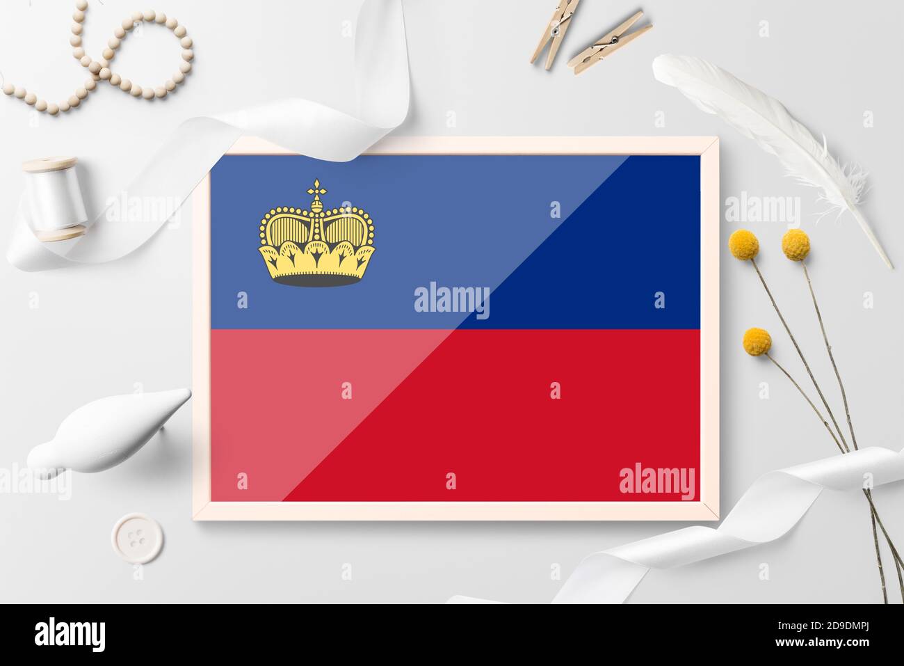 Bandiera Liechtenstein con cornice in legno su sfondo bianco creativo. Tema bianco, piuma, daisy, pulsante, oggetti barra multifunzione. Foto Stock
