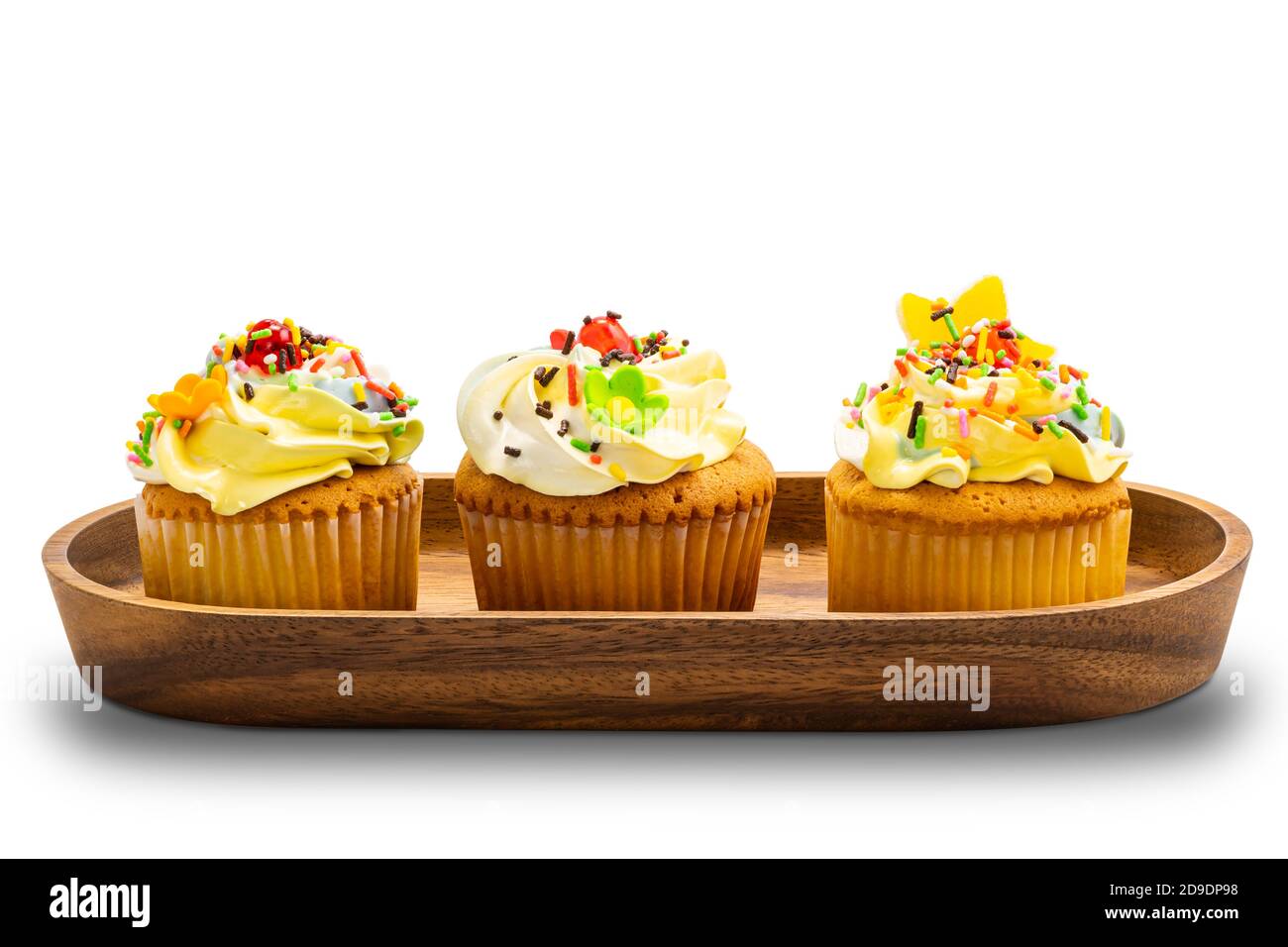 Torte di tazza di vaniglia con crema di burro colorata e spolverate multicolore in vassoio di legno su sfondo bianco con percorso di ritaglio. Foto Stock