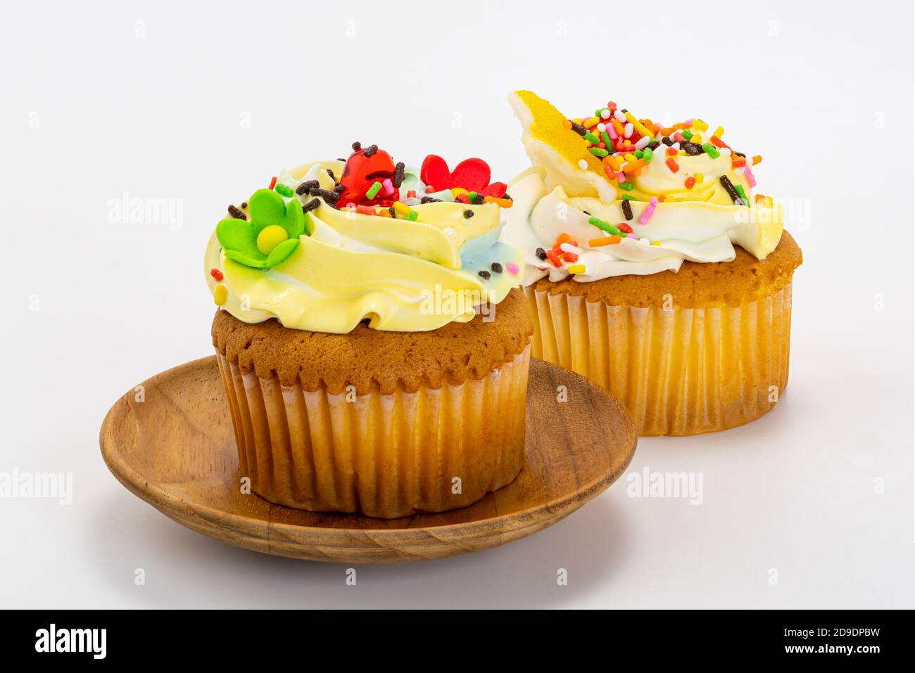 Cupcake alla vaniglia guarnito con gelato alla crema di burro alla vaniglia e spruzzini multicolore in piastra di legno su sfondo bianco con percorso di ritaglio. Foto Stock