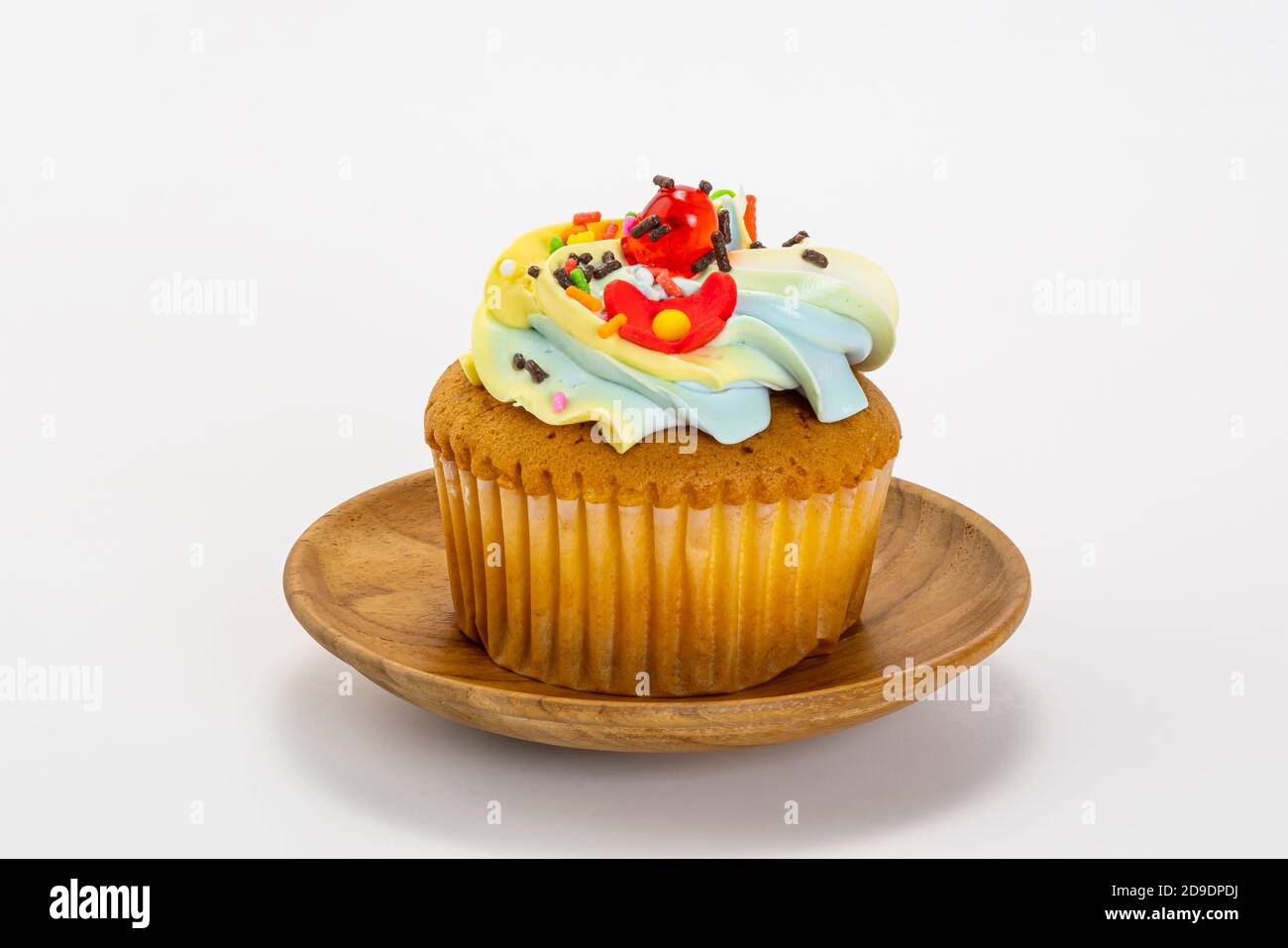 Un singolo cupcake alla vaniglia con crema al burro e glassa decorare con multicolore spruzzare in una piastra di legno isolata su sfondo bianco con ritaglio pa Foto Stock
