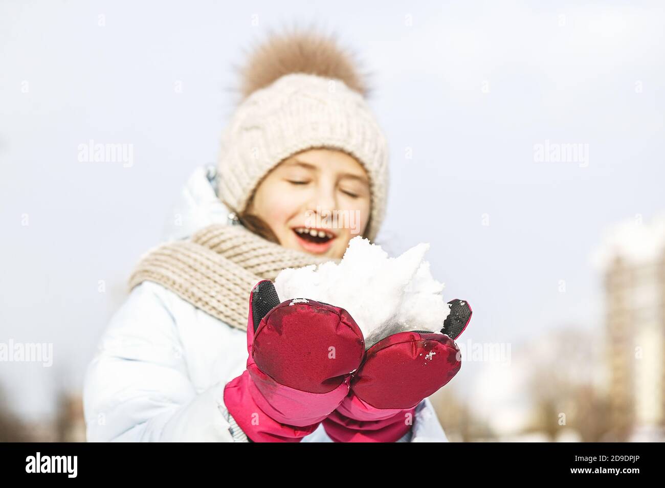 Ritratto invernale di una bella ragazza felice in un cappello invernale lavorato a maglia. Ragazza che tiene la neve. Stile di vita Foto Stock