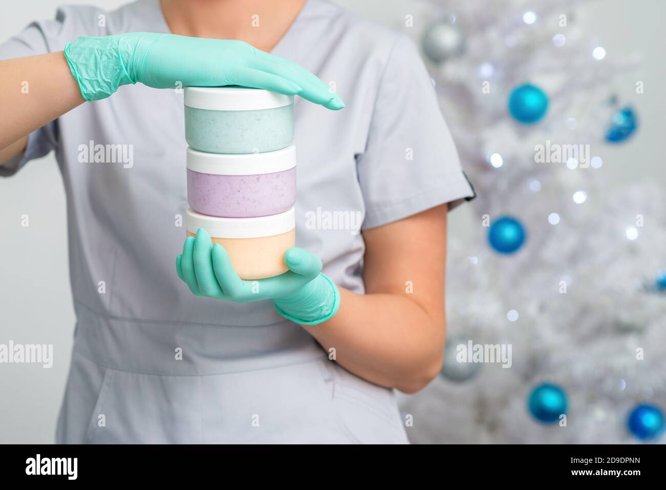 Cosmetologa femminile che tiene tre vasi bianchi con pasta zuccherante sopra albero di natale sfondo Foto Stock