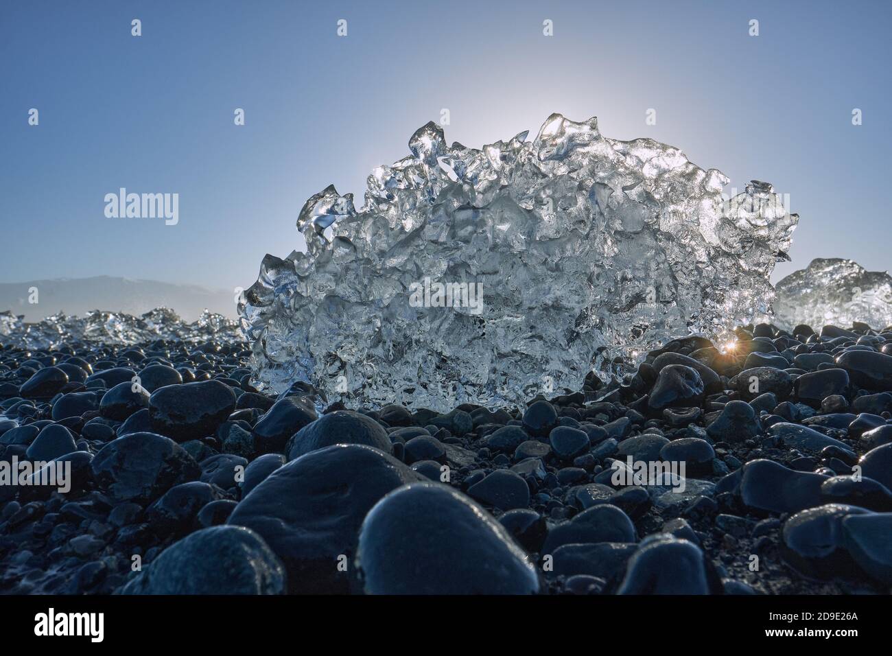Sciogliendo frammenti di iceberg glaciale sulla spiaggia nera di ciottoli basaltici Di Jokulsarlon Islanda - sole che scioglie il ghiaccio - riscaldamento globale - cambiamento climatico Foto Stock