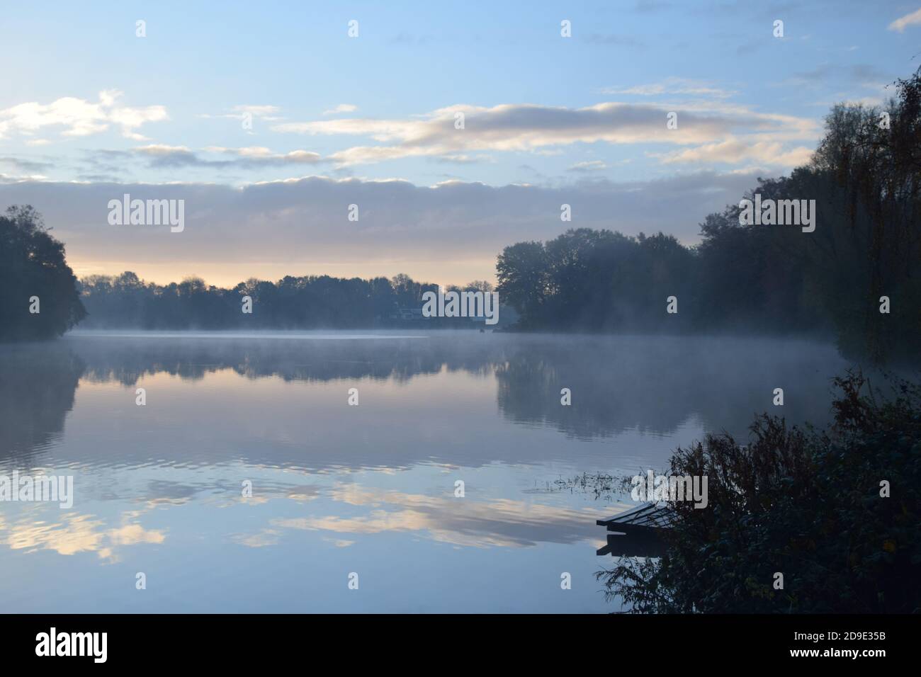 Albe per la prima volta con nebbia persistente sulla superficie dei laghi formare uno specchio che riflette i modelli del cielo sulla sua superficie Foto Stock