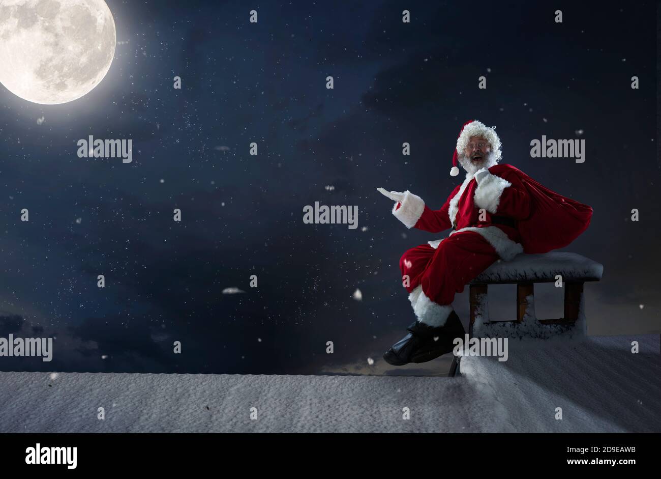 Emotional Babbo Natale congratularsi con Capodanno 2021 e Natale. Uomo in costume tradizionale seduto sul tetto della casa con luna piena su sfondo a mezzanotte. Inverno, vacanze, vendite. CopySpace. Foto Stock