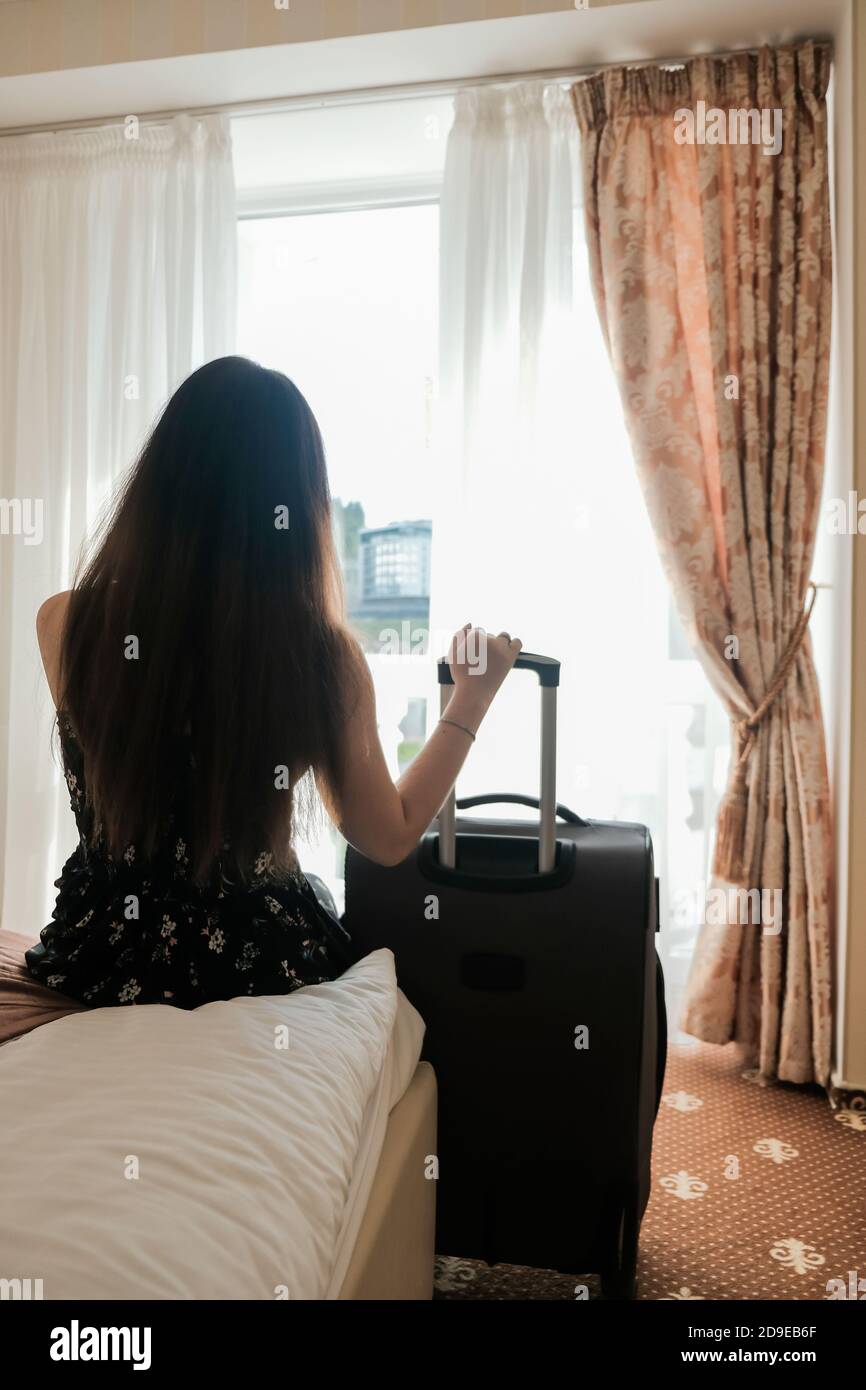 Triste giovane donna con i bagagli pronti a lasciare la camera d'albergo. Ultimo giorno di vacanza. È il momento di tornare a casa. Breve viaggio durante l'isolamento, viaggio limitato Foto Stock