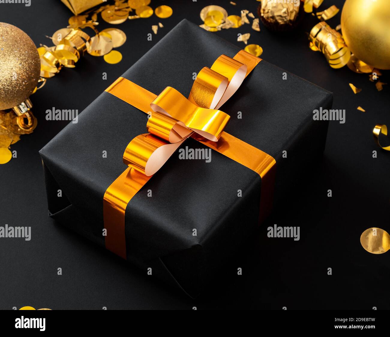 Regalo di natale nero con arco in nastro d'oro e oro natale decorazione festiva su sfondo nero. Buon concetto di anno nuovo su sfondo scuro Foto Stock