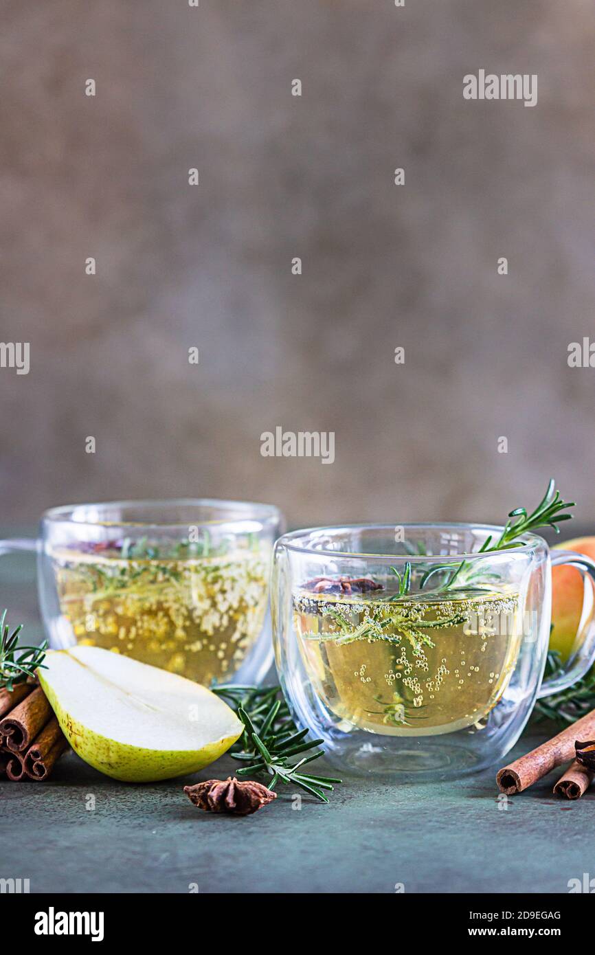 Sidro piccante di pera o mela con cannella, anice e rosmarino. Bevande tradizionali autunnali o invernali. Sfondo verde di cemento. Foto Stock