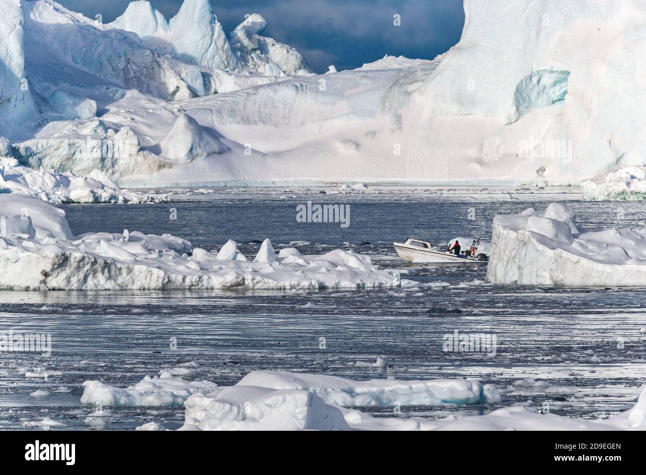 Una barca pescatore sta navigando tra colossali iceberg nel mare Artico. Baia di Disko, Ilulissat, Groenlandia Foto Stock