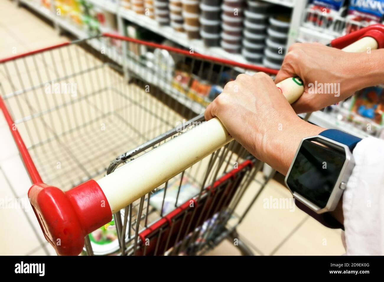 Persona che spinge il carrello del carrello dello shopping contro lo sfondo moderno corridoio del supermercato Foto Stock