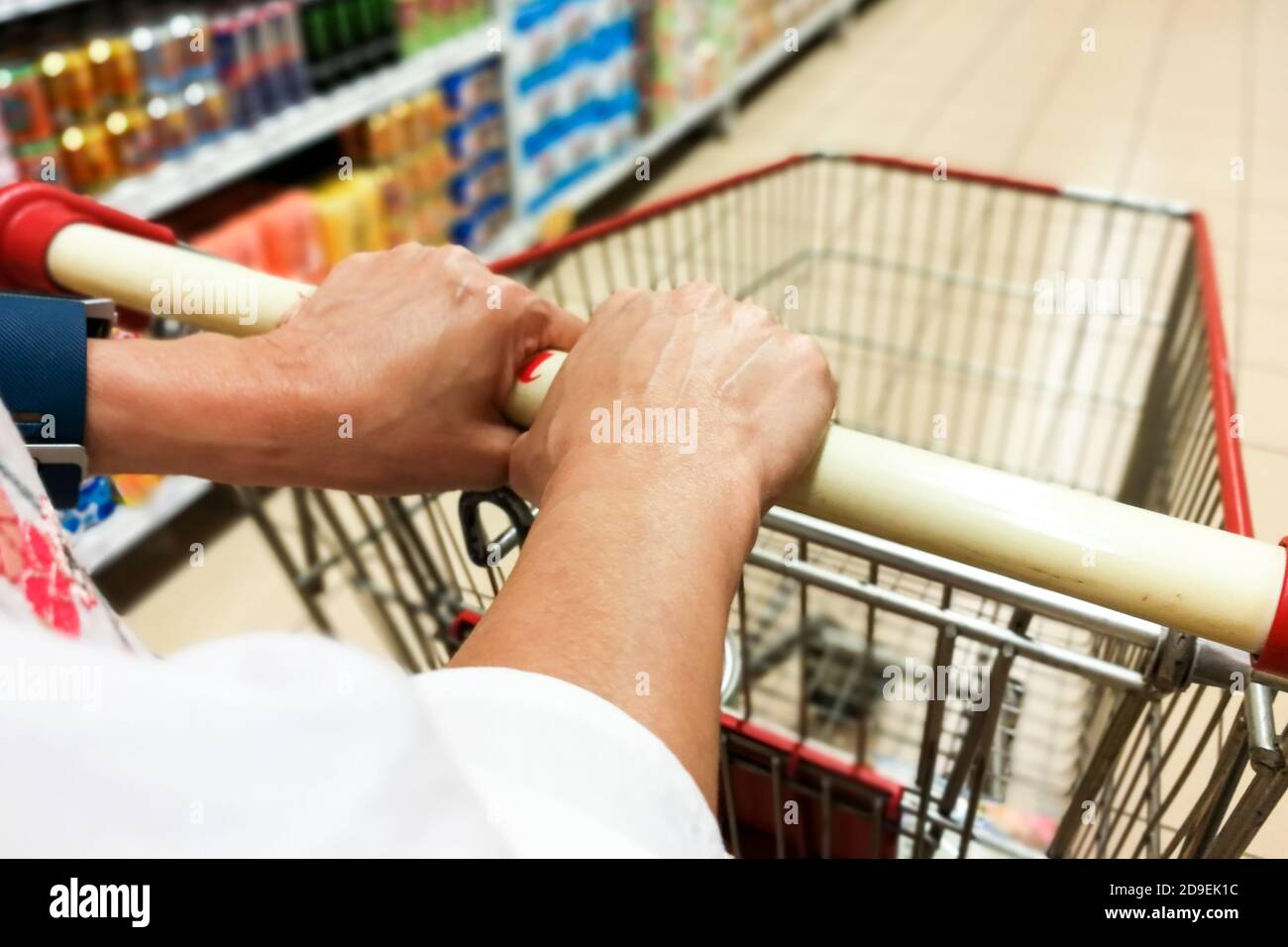 Persona che spinge il carrello del carrello dello shopping contro lo sfondo moderno corridoio del supermercato Foto Stock