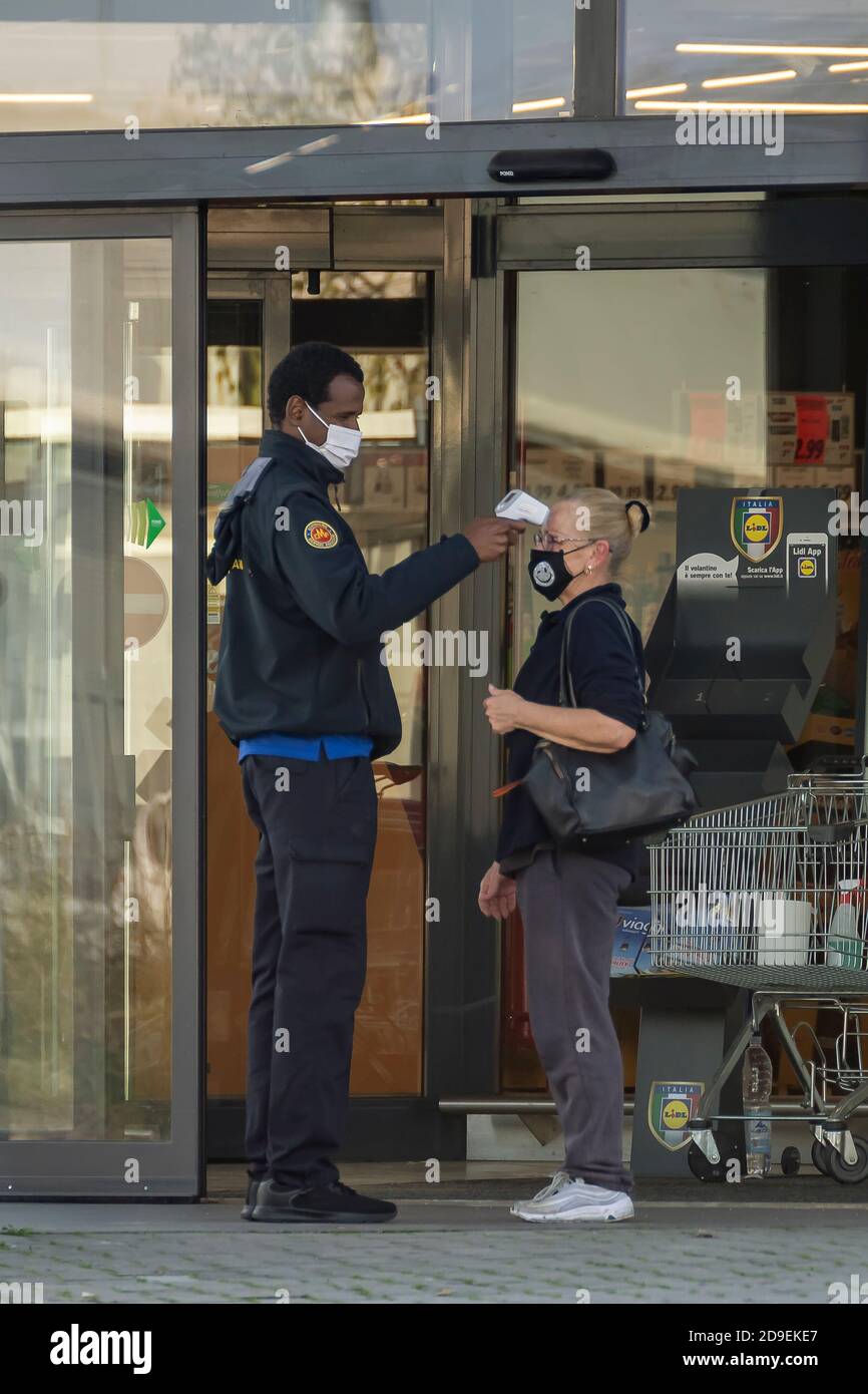 Un responsabile della sicurezza misura la temperatura di un cliente con un digitale termometro a infrarossi per fronte all'ingresso di un supermercato Foto Stock