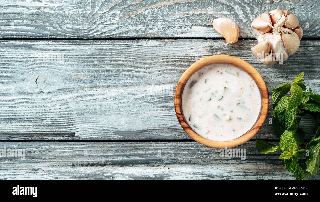 Autentica salsa raita di cetrioli pakistani su sfondo grigio di legno. Condire la salsa raita con cetrioli, cipolla e pomodoro in una piccola ciotola di metallo e in un vasetto di vetro. Vista dall'alto o piatta. Spazio di copia. Banner Foto Stock