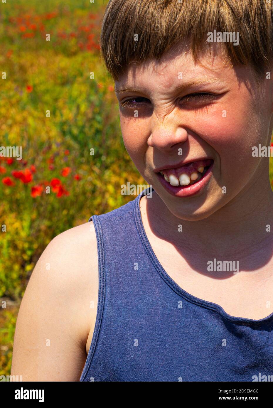 Il ragazzo squinted e sorride contro lo sfondo di campi di papavero. Estate. Vacanze. Molto sole e buon umore. Foto Stock