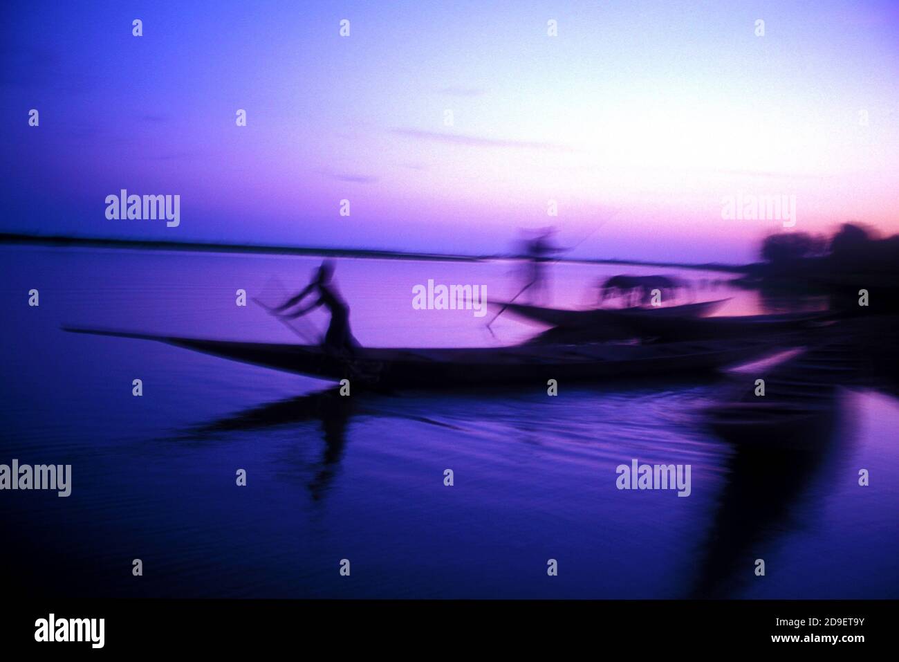 Barche di pescatori sfocate che attraversano il fiume Niger nel Mali al tramonto. Foto Stock