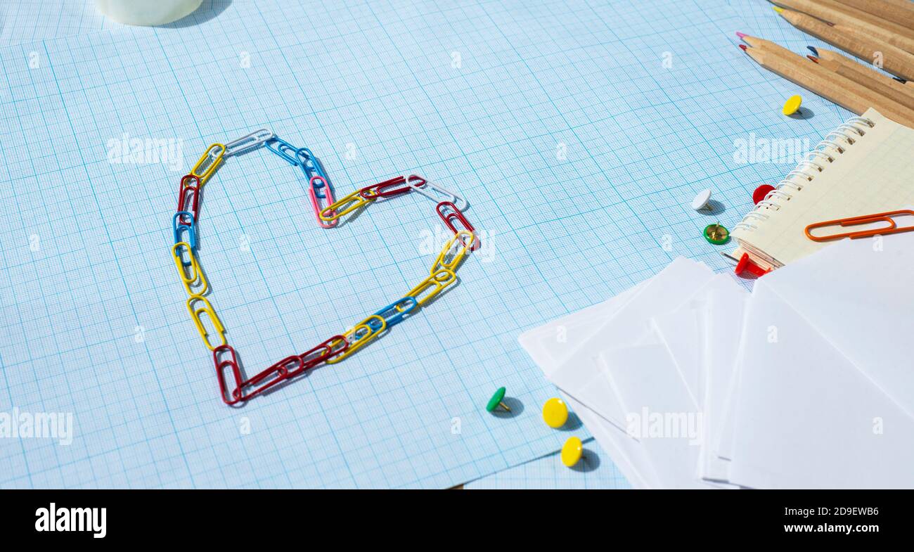 Matite dei perni di spinta della carta e un cuore fatto di fermagli di carta colorati. Spazio libero per il testo. Foto Stock