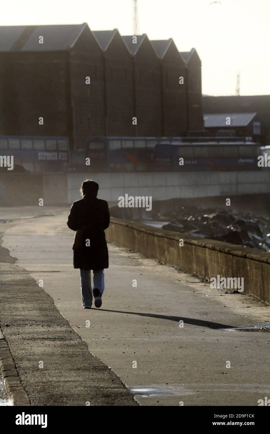 Newton Shore, Ayr, Ayrshire, Scozia, Regno Unito. Donna che cammina lungo il mare in giornata ventosa Foto Stock