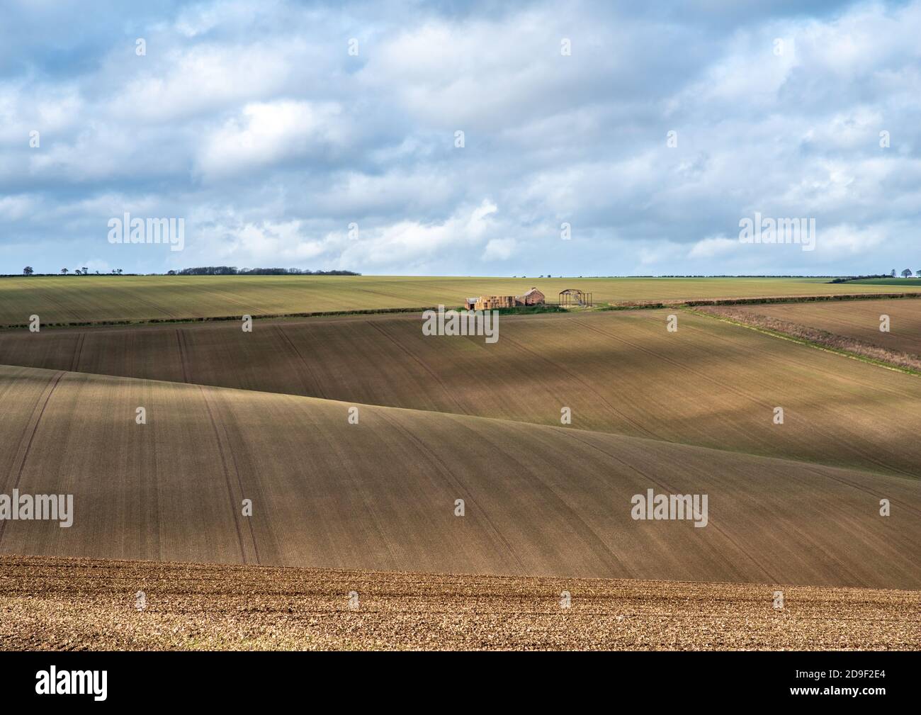 Vista di una fattoria derelict su campi ondulati arati a strisce in una giornata di sole con cielo nuvoloso. Foto Stock