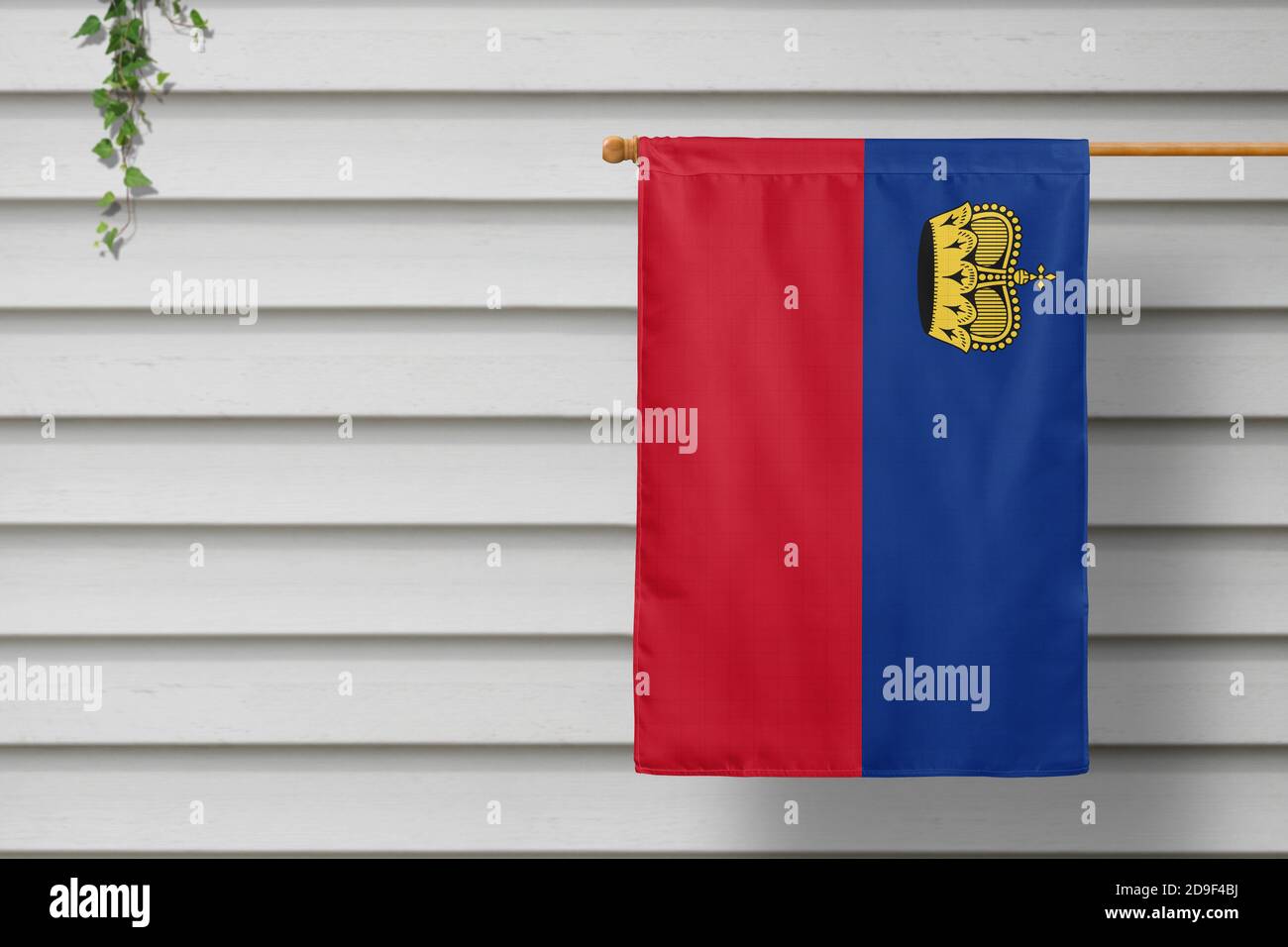 La piccola bandiera nazionale del Liechtenstein pende da una recinzione per picnic lungo il muro di legno in una città rurale. Concetto di giorno di indipendenza. Foto Stock