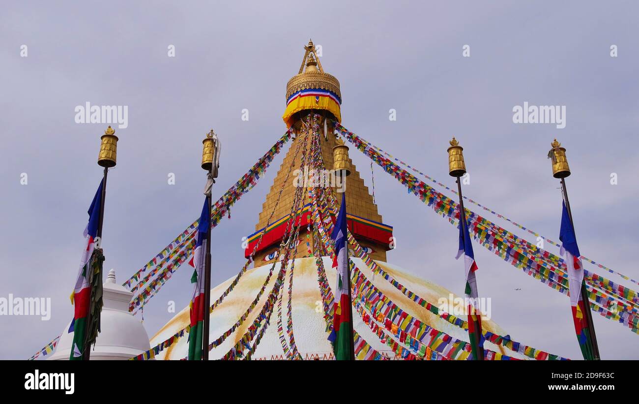 Cima della famosa Boudhanath stupa (Boudha) nel centro di Kathmandu, Nepal, decorato con colorate bandiere di preghiera buddista e cinque lampioni. Foto Stock