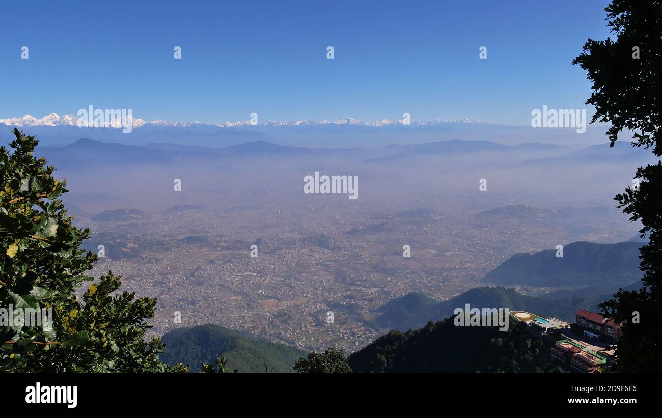 Splendida vista panoramica sulla valle di Kathmandu, Nepal con fumo visibile sopra la città, la maestosa catena montuosa Himalaya e un resort di lusso per le vacanze. Foto Stock