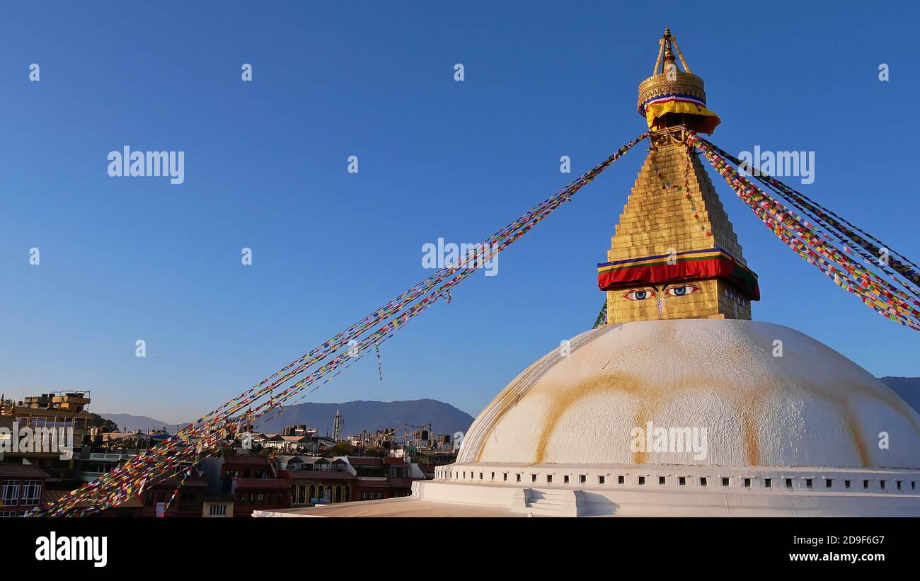 Enorme Boudhanath stupa (Boudha) nel centro di Kathmandu, Nepal decorato con colorate bandiere buddiste di preghiera con edifici e colline Himalaya. Foto Stock