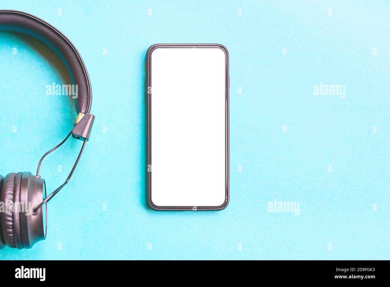Cuffie e smartphone su sfondo blu. Foto trendy. Flat Lay Concept: Dispositivi per la vita di tutti i giorni. Stile minimalista con sfondo di carta colorato. Telefono con schermo vuoto, spazio per la copia. Foto Stock