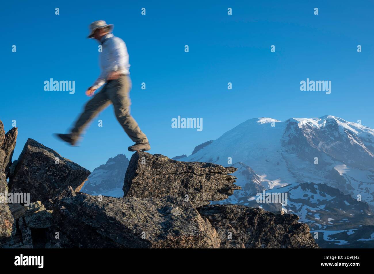 Uomo che attraversa due rocce con Mt Rainer in distanza Foto Stock
