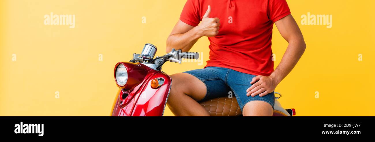 vista ritagliata di un uomo seduto su uno scooter rosso e mostrante pollice su giallo Foto Stock
