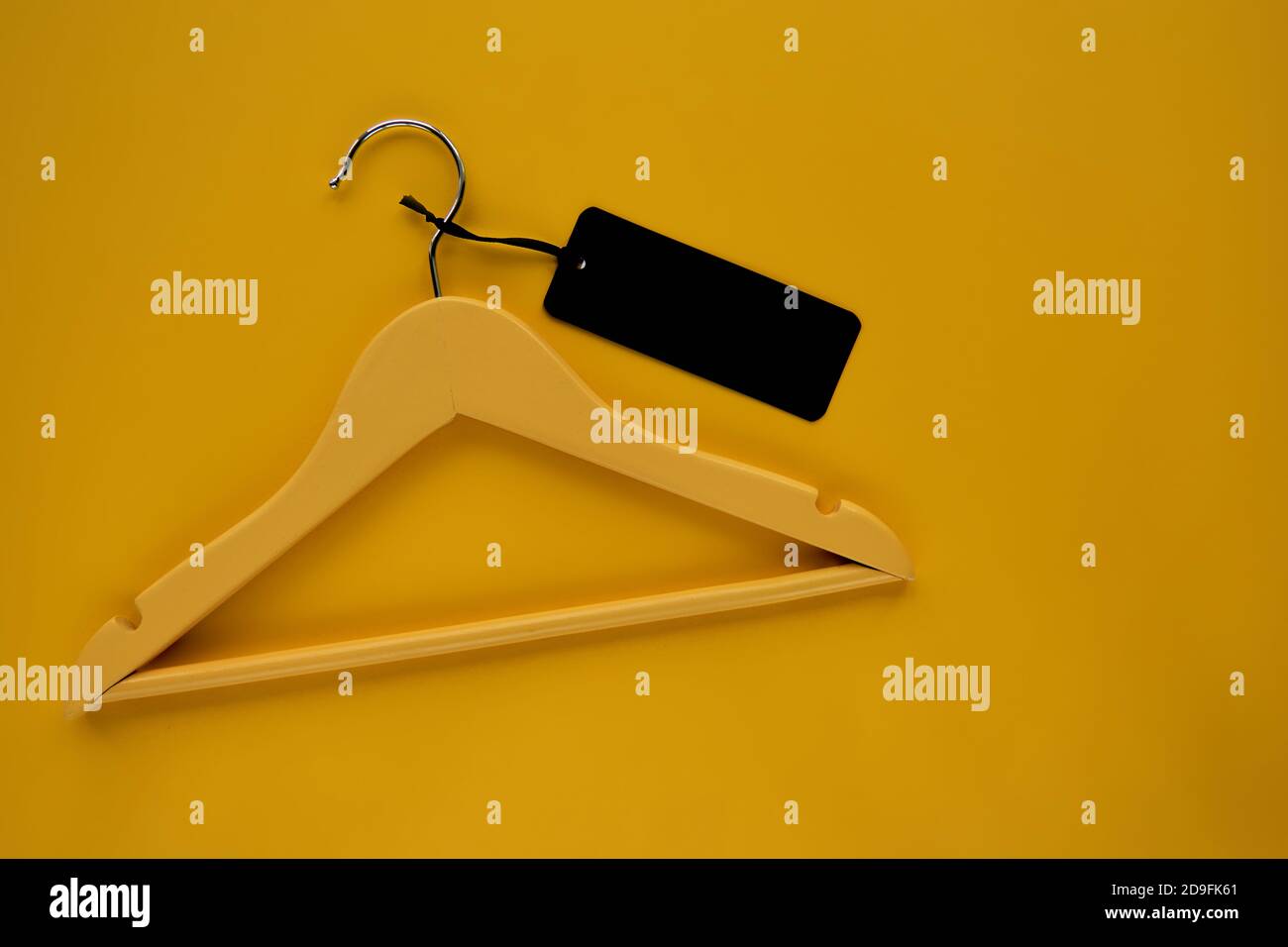 Appendiabiti in legno con etichetta di carta nera isolata su sfondo di carta giallo. Etichetta di abbigliamento, etichetta modello mockup vuoto, per posizionare il tuo disegno. Nero Foto Stock