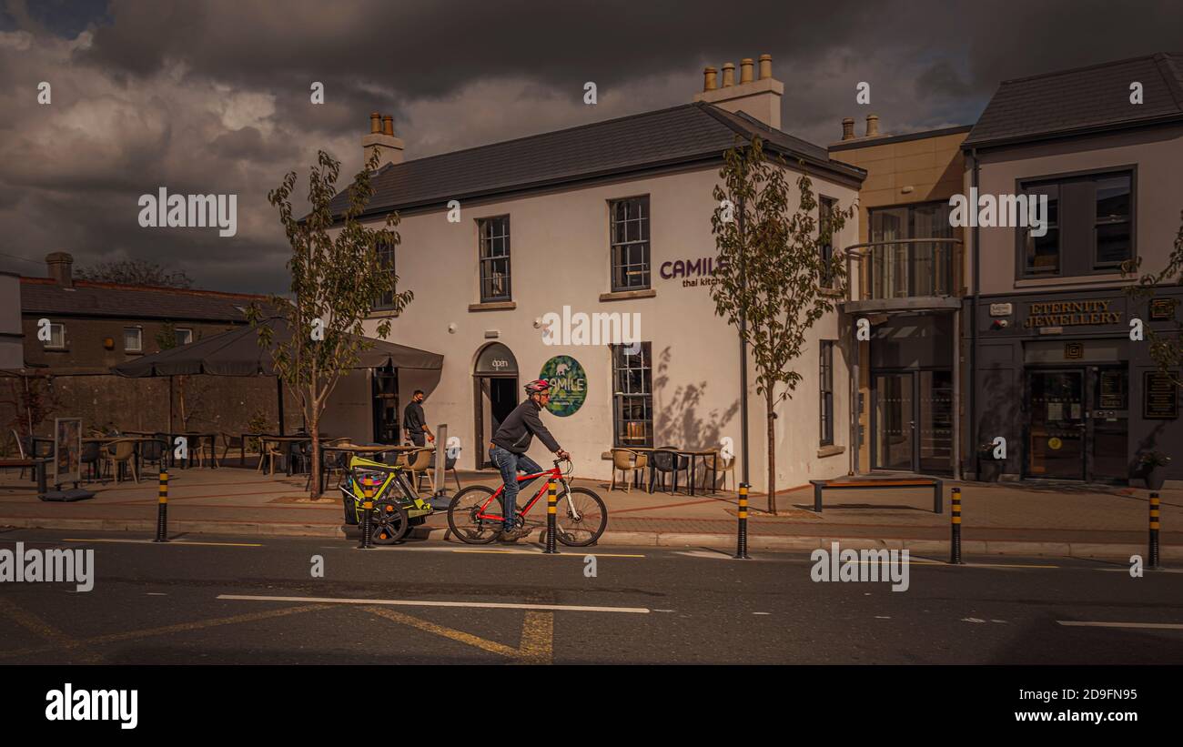 Vita quotidiana. Uomo in bicicletta con rimorchio per bambini attaccato alla moto. Foto Stock