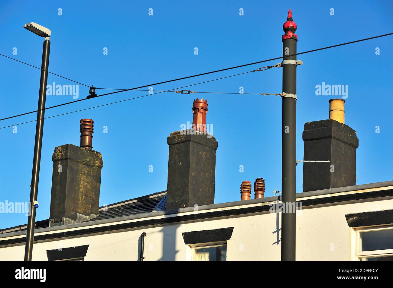 Pile di camini nero opaco, palo della lampada e palo del cavo sospeso contro cielo blu Foto Stock