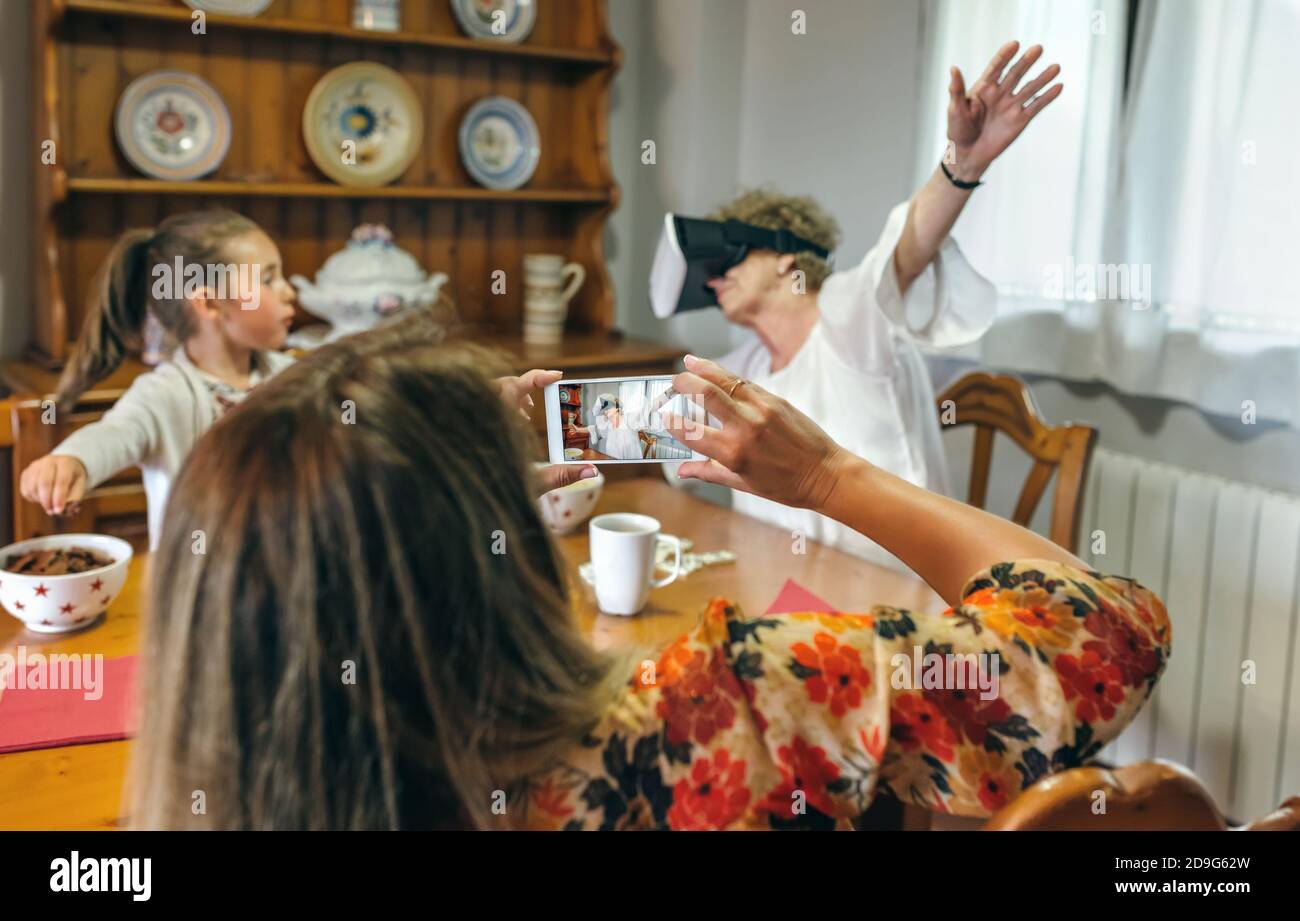 Giovane donna scattando una foto a sua madre usando virtuale occhiali reality Foto Stock