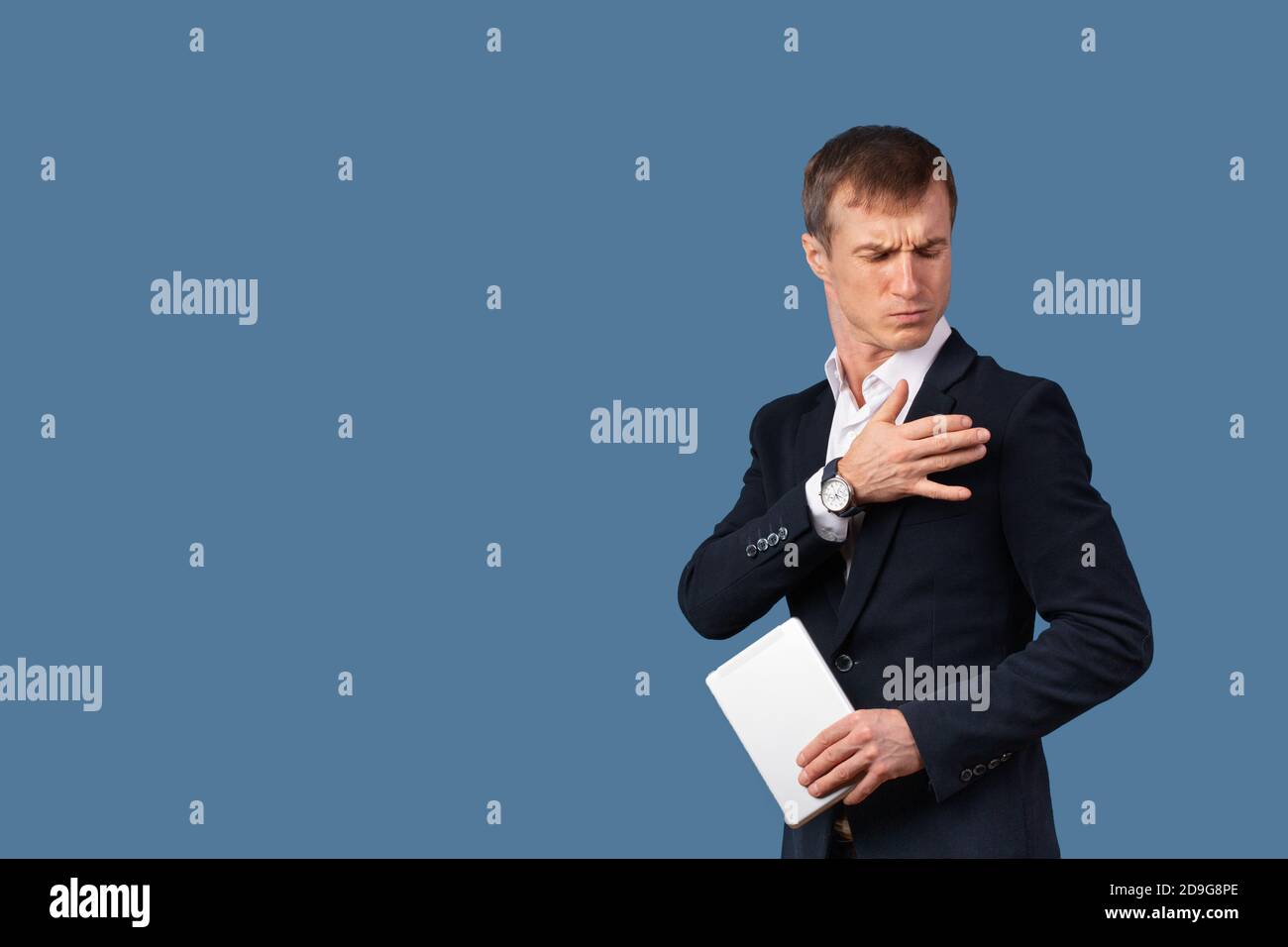 Un uomo d'affari maschile arrogante in un vestito scuote la polvere dai vestiti e dalle spalle con disprezzo. Studio girato su sfondo blu con spazio per tex Foto Stock