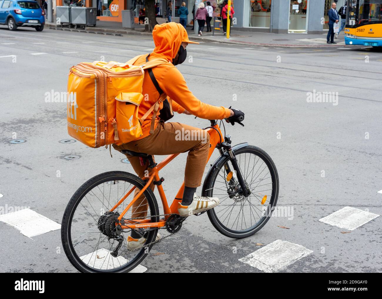 Corriere di consegna di fast food maschile che indossa il vestito arancione della compagnia da asporto con la bicicletta in strada trafficata a Sofia, Bulgaria, Europa orientale, Balcani, UE Foto Stock