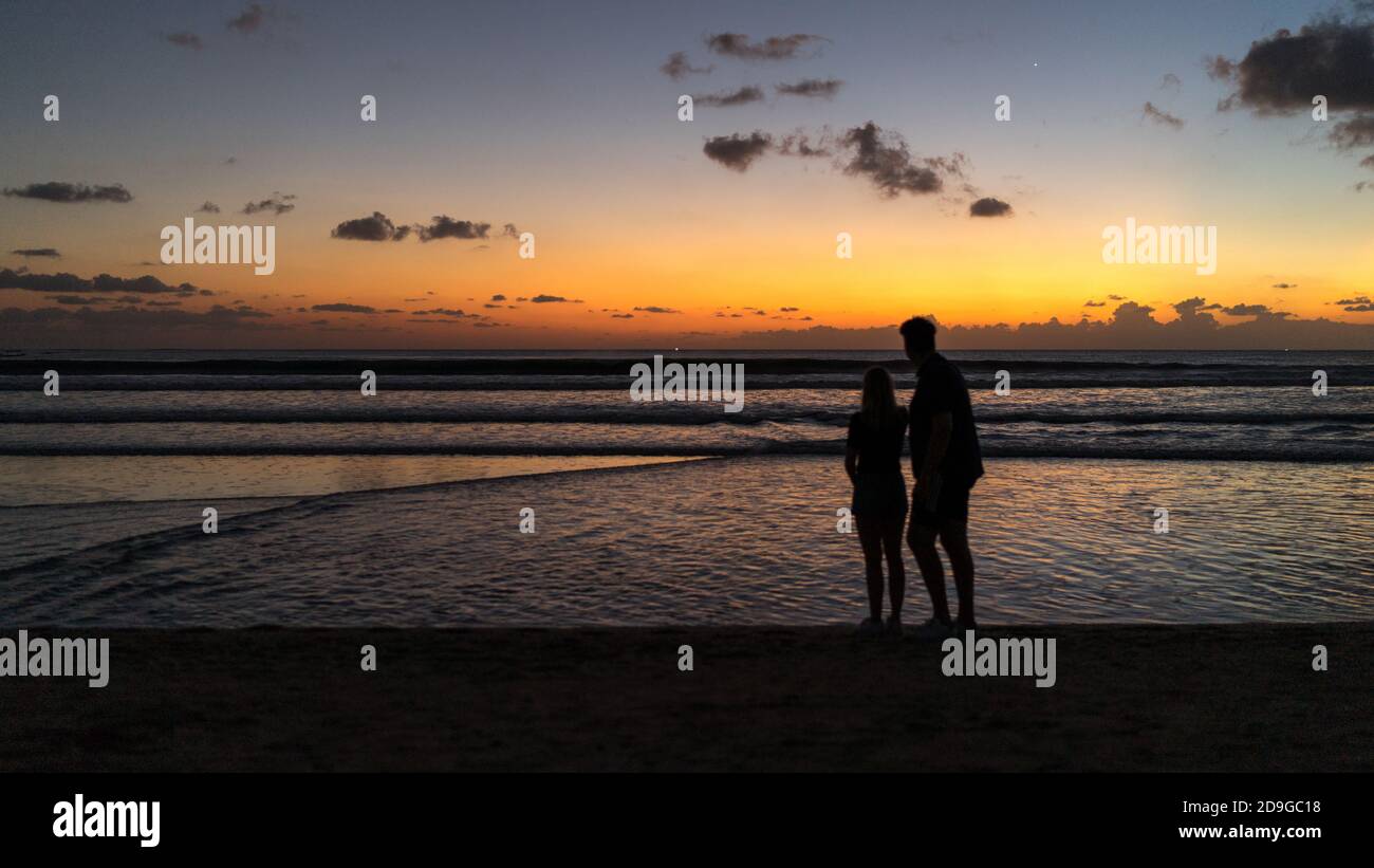Coppia che cammina sulla spiaggia al tramonto, una silhouette di una coppia sulla spiaggia guardando il tramonto dorato a Kuta, Bali Foto Stock