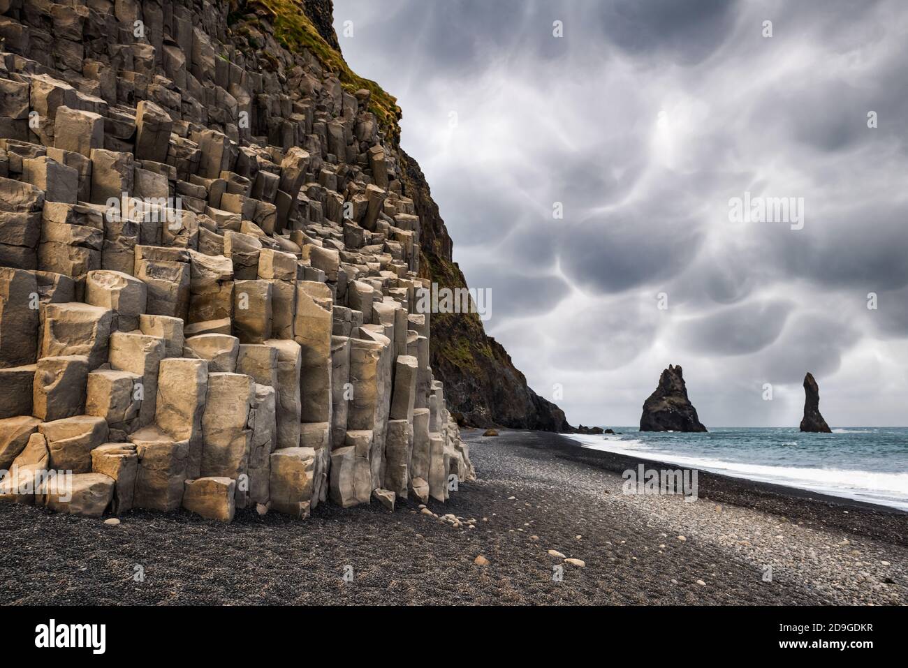 Vista incredibile sulla spiaggia nera e le scogliere di Troll Toes in tempo nuvoloso. Cielo tempestoso con minacciose nuvole di mammato sullo sfondo. Reynisdrangar, Vik, Islanda. Fotografia di paesaggio Foto Stock