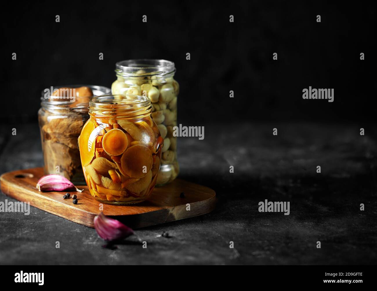 Vasetto di vetro con funghi in scatola con aglio e pepe. Cibo fermentato su sfondo scuro con spazio di copia Foto Stock