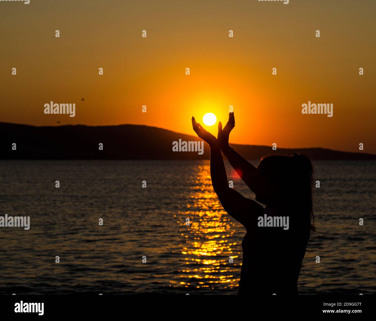 La ragazza tiene il sole nelle sue mani. Bellissima alba sul mare Foto Stock